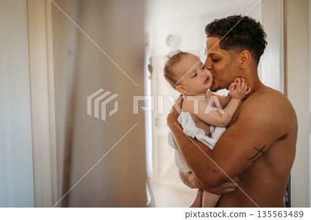 Father and small baby son wrapped in towel after bath. 135563489