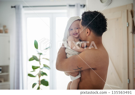 Father and small baby son wrapped in towel after bath. 135563491