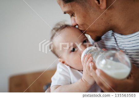 Father bottle feeding a small toddler son. 135563503