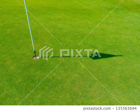 Golf hole with a flag on a lush green putting green during a bright sunny day. Golf hole with a flag on a lush green putting green during a bright sunny day. 135563694