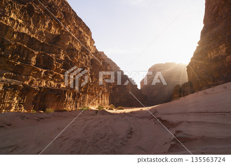 Sunrise light reveals rocky canyon with soft sand at the base in the desert. Wadi Rum desert, Jordan Sunrise light reveals rocky canyon with soft sand at the base in the desert. Wadi Rum desert, Jordan 135563724
