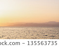 Sunset over the water with distant mountains and birds flying in the sky 135563735