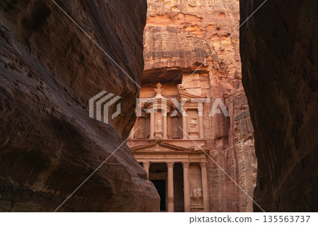 View of ancient structure in Petra surrounded by tall rock formations at sunset time 135563737