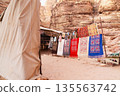 Colorful fabrics hang on display near rock formations in a warm desert location. Petra, Jordan. 135563742