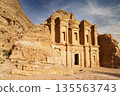 Ancient structure stands tall against rugged mountains during sunset. Ed-Deir - Nabatean Monastery, Petra, Jordan. 135563743