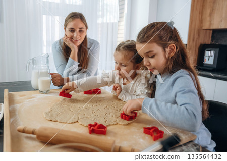 Preparing bakery. Mother with her little daughters at home Preparing bakery. Mother with her little daughters at home 135564432