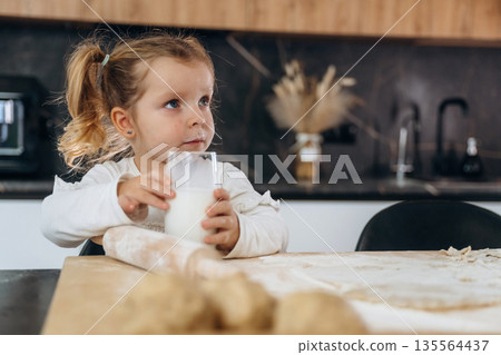 With milk in glass. Little girl is preparing bakery at home 135564437