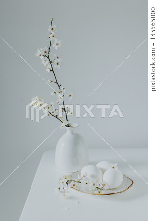 Beautiful branches with white blossom and eggs on a white table. Minimal Easter concept. Beautiful branches with white blossom and eggs on a white table. Minimal Easter concept. 135565000