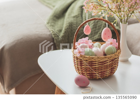 Easter Basket with Ester Eggs,  Plush Bunny and Spring Decor on White Table intoCozy Living Room 135565090
