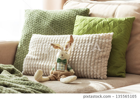 Cozy Sofa with Plush Easter Bunny Doll and Textured Pillows in Sunlight Cozy Sofa with Plush Easter Bunny Doll and Textured Pillows in Sunlight 135565105