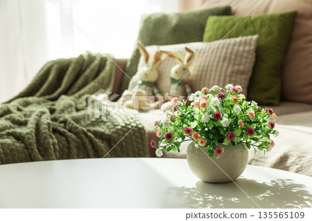Cozy Easter Living Room with Plush Easter Bunny Dolls and Spring Flowers on Table 135565109