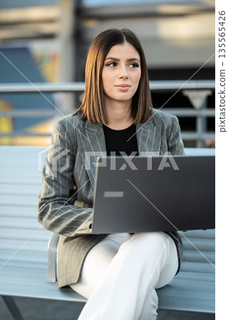 Young businesswoman working on a laptop outdoors in the city, remote freelancer contemplating ideas for professional growth, modern connectivity and urban entrepreneurship Young businesswoman working on a laptop outdoors in the city, remote freelancer contemplating ideas for professional growth, modern connectivity and urban entrepreneurship 135565426