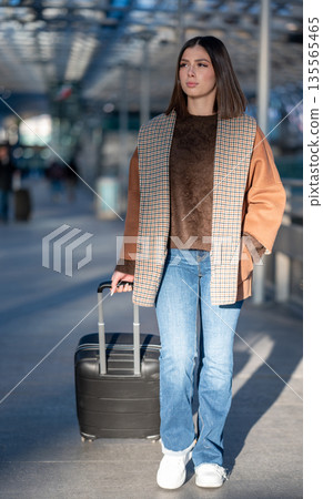 Young woman walking and pulling a suitcase, preparing for travel or returning home, depicting concepts of journey, exploration, and modern lifestyle in an urban environment Young woman walking and pulling a suitcase, preparing for travel or returning home, depicting concepts of journey, exploration, and modern lifestyle in an urban environment 135565465
