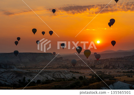 Hot air balloon flying over rocky landscape at sunrise in Cappadocia. Turkey Hot air balloon flying over rocky landscape at sunrise in Cappadocia. Turkey 135565501