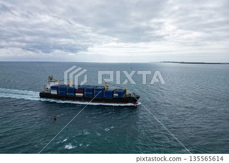 Cargo ship in sea, aerial view. Freight container loaded on cargo vessel. Aerial view cargo ship entering harbor. Cargo business. Container ship at seascape. Shipping logistics. Commercial shipping Cargo ship in sea, aerial view. Freight container loaded on cargo vessel. Aerial view cargo ship entering harbor. Cargo business. Container ship at seascape. Shipping logistics. Commercial shipping 135565614