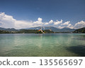 Scenic view of Lake Bled with iconic island church, clear turquoise water and alpine mountains under blue sky on a sunny summer day in Slovenia 135565697
