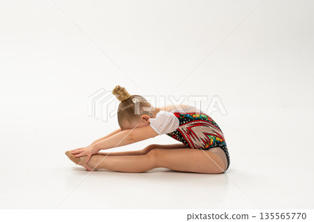 Side view of gymnast with cochlear implant stretching in studio leotard. Hearing rehabilitation, posture control and inclusive childhood physical development through rhythmic training 135565770