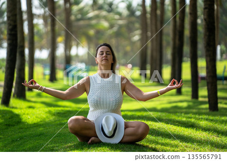 A girl sits in the lotus position on a green lawn and catches zen in yoga A girl sits in the lotus position on a green lawn and catches zen in yoga 135565791
