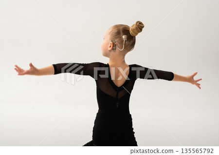 Little girl in black latin dance dress performing graceful pose with cochlear implant. Copy space. Overcoming hearing loss through movement, inclusion, and confidence in art and rhythmic self 135565792