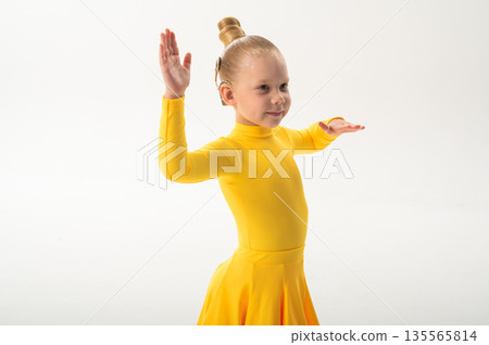 Little girl in yellow dress dancing with cochlear implant. Overcoming hearing loss through rhythm, art, inclusion, and strength of spirit in artistic gymnastics and ballroom dance. 135565814