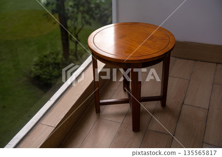 A round table sits on beige tiles next to a glass window A round table sits on beige tiles next to a glass window 135565817