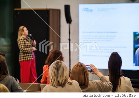 Female speaker presents at conference while audience watches and records on smartphone Female speaker presents at conference while audience watches and records on smartphone 135565859