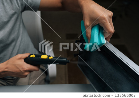 Close-up of unrecognizable man cleaning microwave oven using handheld steam cleaner, applying hot vapor to disinfect and remove grime, maintaining hygiene in kitchen appliance with modern tools. Close-up of unrecognizable man cleaning microwave oven using handheld steam cleaner, applying hot vapor to disinfect and remove grime, maintaining hygiene in kitchen appliance with modern tools. 135566002