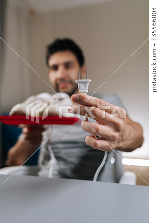 Vertical focus on foreground of blurred male holding electric plug for shoe dryer, preparing to clean and dry white sneakers, focusing on home care routine and footwear maintenance. 135566003
