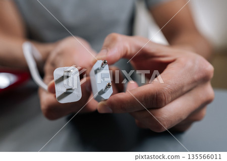 Male hands holding electrical plug with uk type g connector and european type c travel adapter, illustrating power compatibility for charging devices while traveling internationally. Male hands holding electrical plug with uk type g connector and european type c travel adapter, illustrating power compatibility for charging devices while traveling internationally. 135566011