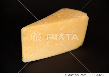 piece of hard cheese. Appetizing cheese isolated on black background close-up 135566419