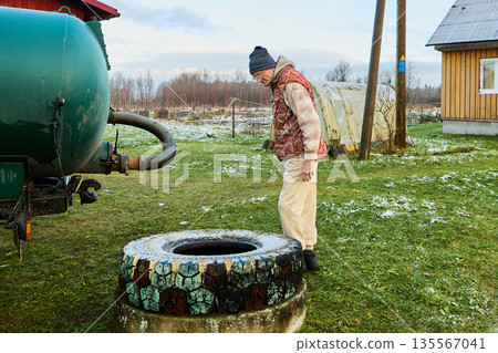 Sanitation worker operating sewage vacuum truck hose near rural cesspit emptier opening during routine waste removal process at homestead. Sanitation worker operating sewage vacuum truck hose near rural cesspit emptier opening during routine waste removal process at homestead. 135567041