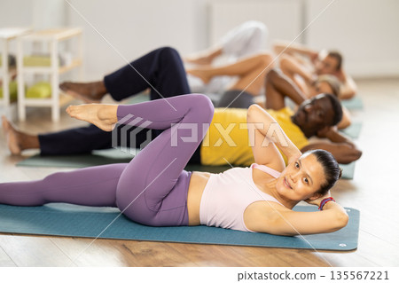 Group of multinational people doing exercises for press during group class in fitness studio Group of multinational people doing exercises for press during group class in fitness studio 135567221