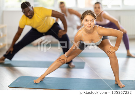 Girl conducts fitness pilates training for multinational students, performs standing exercises 135567222