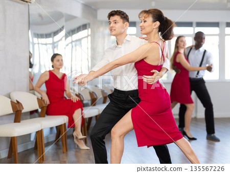 Hispanic guy and woman in red engrossed in passionate tango during dance class 135567226