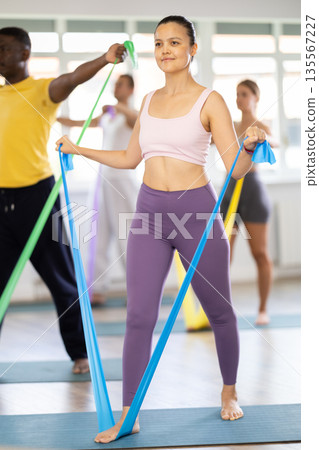 Group of athletes train in Pilates class using elastic bands 135567227