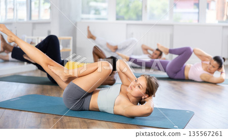 Multinational Pilates participants pulls elbows up to opposite knee, performs exhausting exercises Multinational Pilates participants pulls elbows up to opposite knee, performs exhausting exercises 135567261