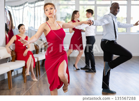 Cheerful female practicing lindy hop in pair with African american man in dance salon 135567288
