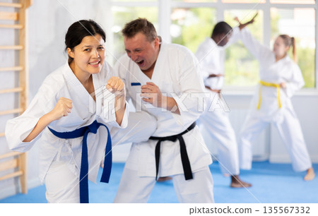 Woman and man in kimono and belts sparring during karate training Woman and man in kimono and belts sparring during karate training 135567332
