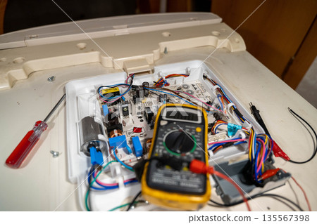 Close-up view of an open electronic device revealing intricate circuit board components, multimeter, and tools on a work surface during a repair process 135567398