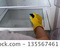 Person wearing yellow rubber gloves is cleaning the interior of a refrigerator with a sponge, showcasing a clear and organized space during a cleaning session 135567461