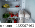 Open refrigerator filled with fresh produce including bananas, red peppers, cucumbers, and eggs arranged neatly in a clear container on a shelf for easy access and organization 135567463