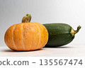 Orange pumpkin and green zucchini placed on a light surface with a soft gradient background, showcasing their natural textures and colors for culinary or seasonal use 135567474