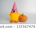 Cute plush toy character with a pink party hat is sitting next to a small orange pumpkin on a light background, ideal for autumn-themed decorations or children's events 135567478