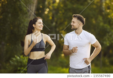 Happy couple sporty fit running in green park on sunny day, jogging leisurely, expressing shared joy Happy couple sporty fit running in green park on sunny day, jogging leisurely, expressing shared joy 135567490