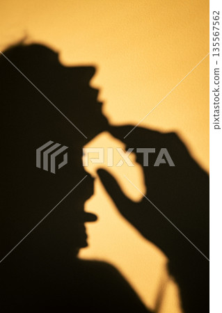 A high-contrast silhouette of female face in profile and a hand on a sunlit yellow wall. A minimalist abstract shot. A girl in silhouette. A high-contrast silhouette of female face in profile and a hand on a sunlit yellow wall. A minimalist abstract shot. A girl in silhouette. 135567562
