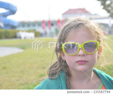 A sweet little girl wearing sunglasses at the pool. A smiling little girl wearing a beach towel at the pool. Happy kid at aqua. Little girl in sunglasses on a summer sunny day. Summer holiday concept A sweet little girl wearing sunglasses at the pool. A smiling little girl wearing a beach towel at the pool. Happy kid at aqua. Little girl in sunglasses on a summer sunny day. Summer holiday concept 135567744