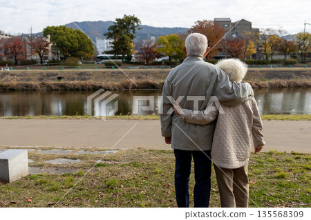 A friendly, gray-haired elderly couple looking out over the Kamo River in Kyoto 135568309