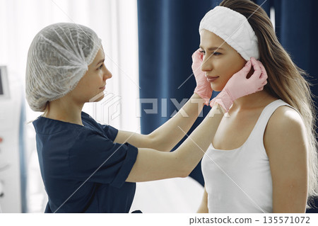 Cosmetologist puts a bandage on the client. Woman with cosmetologist. Lady in a beauty studio. Cosmetologist puts a bandage on the client. Woman with cosmetologist. Lady in a beauty studio. 135571072