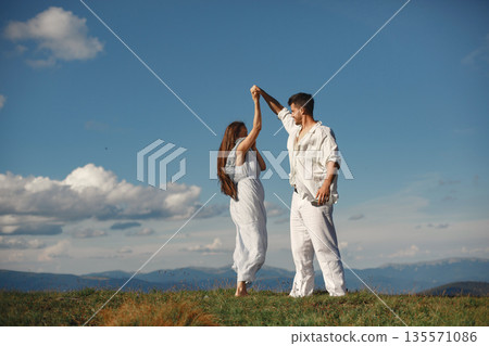 Man and woman in the mountains. Young couple in love at sunset. Woman in a blue dress. Peopel standing on a sky background. Man and woman in the mountains. Young couple in love at sunset. Woman in a blue dress. Peopel standing on a sky background. 135571086