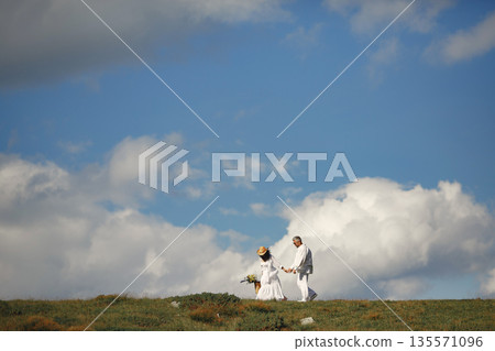 Senior man and woman in the mountains. Woman with basket of flowers. Man in a white shirt. 135571096